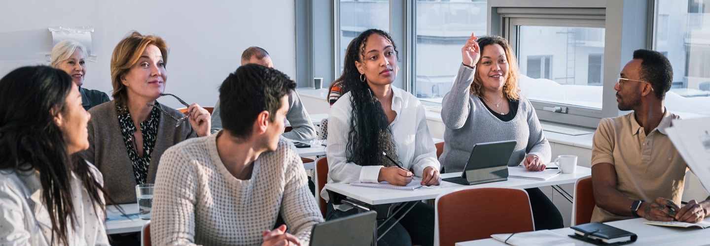 People studying in a classroom with one holding her hand up