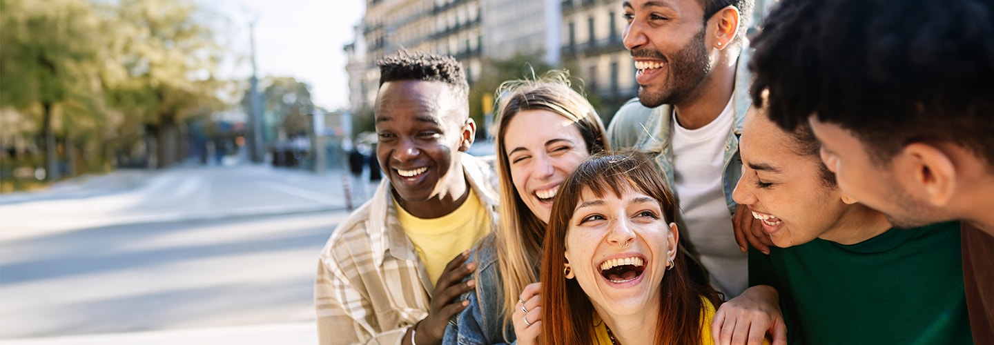 Five people walking together on a sunny city street, displaying casual, comfortable clothing and diverse hairstyles.